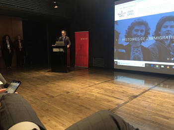 A man speaks on the podium and the people below are watching him
